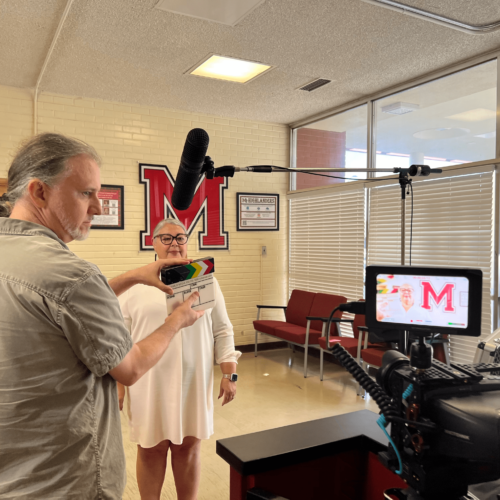 A woman prepares to give an interview in front of a microphone and videographer