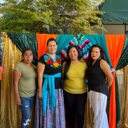 A group of women pose in front of a colorful curtain for hispanic heritage month