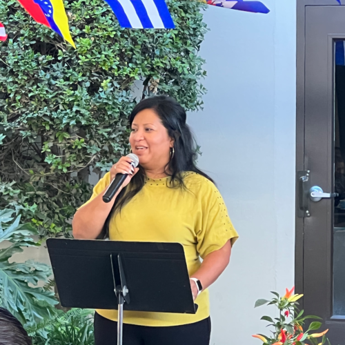 A woman in a yellow shirt speaks into a microphone during a presentation