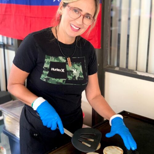A woman smiles at the camera while cooking on a flattop