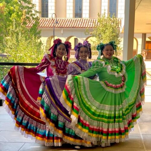Three women in traditional dresses celebrate Hispanic heritage month